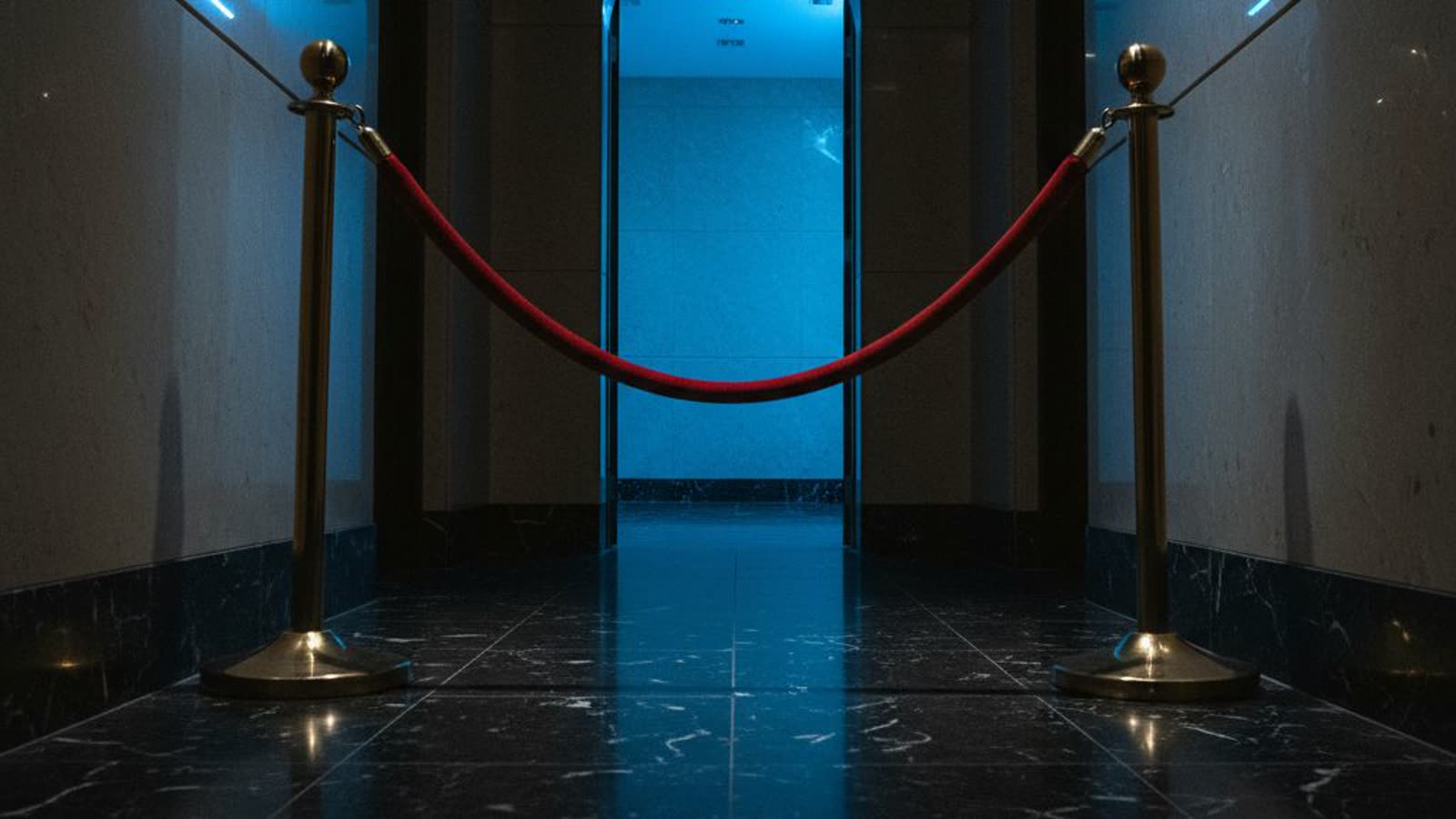 An open doorway in a dark marble hallway with a red velvet rope still hooked across it.
