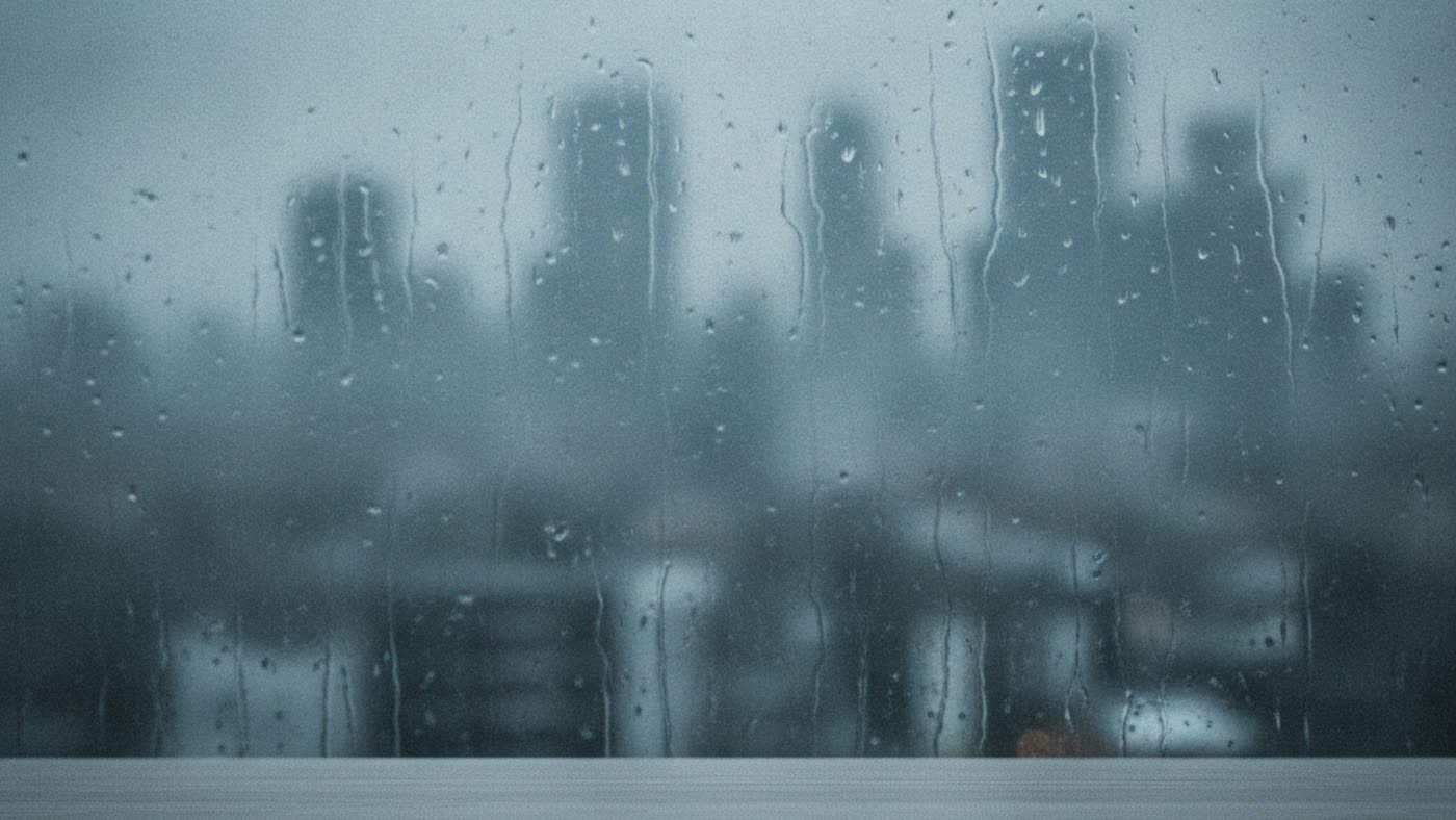 A rain-streaked window with a blurred city skyline behind it.